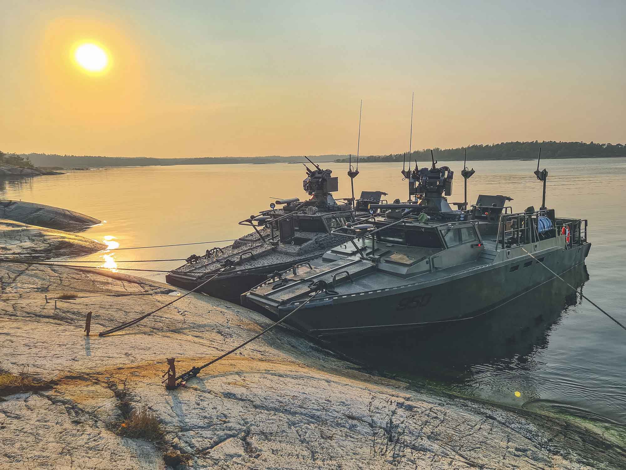 Två stridsbåtar ligger vid en klippa i solnedgång.