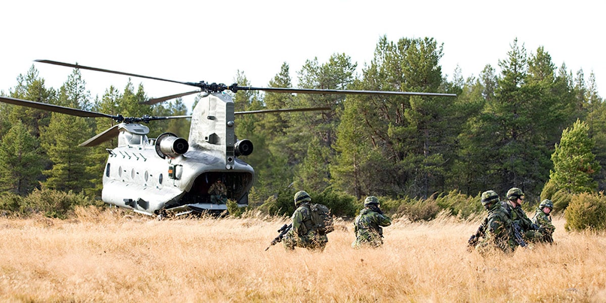Soldiers in high grass moving towards a helicopter in the terrain
