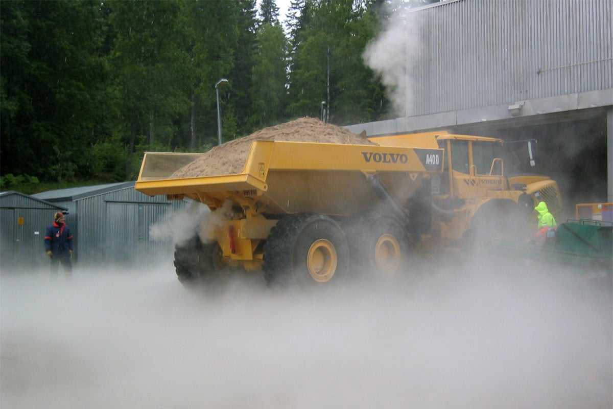 A yellow Volvo dumper with mist around it, in front of a building 