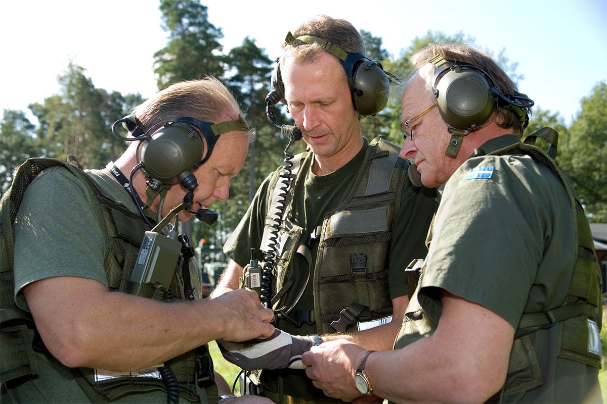 Three men with ear protectors looking concentrated at something in their hands